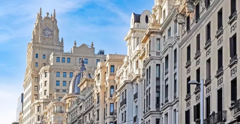 Madrid's city street showcases tall buildings and a prominent clock tower; one of the top 3 European cities to invest in.