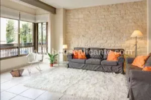 A centrally-located apartment in Alicante with a stone wall and orange furniture.