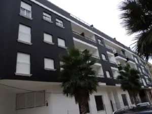 A black apartment building with palm trees parked in front of it.