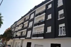 A black and white apartment building with balconies and palm trees.