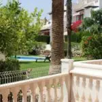 A townhouse in Villamartin with a white fence, palm trees, and a swimming pool for less than 100.000€ in Orihuela Costa.