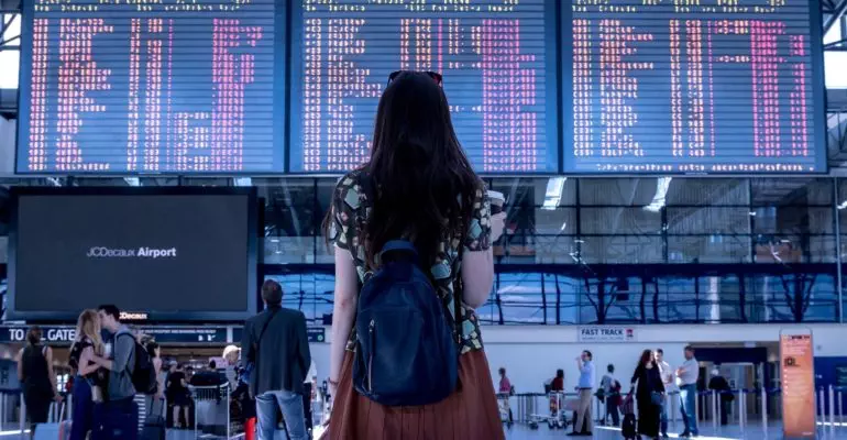 A woman monitors the flight schedule board at an airport, focusing on flights to Spain.