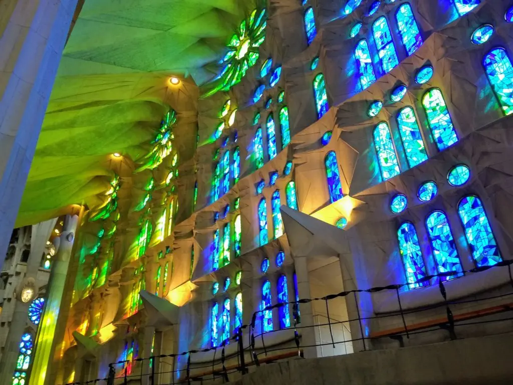 Brilliant stained glass windows bathe Gaudí's sacred columns in cascading waves of red, blue, green, and yellow light, transforming stone into a living kaleidoscope of divine radiance in the Sagrada Familia