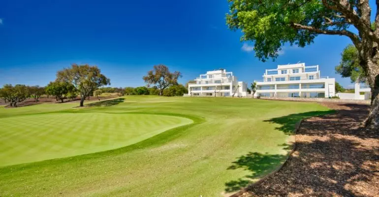 A golf course with trees and buildings in the background, located in Cadiz or San Roque.