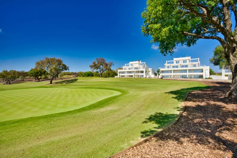 A golf course with trees and buildings in the background, located in Cadiz or San Roque.