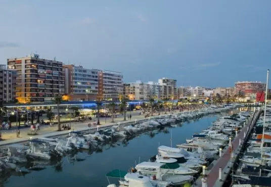 A marina with boats docked in front of buildings at dusk and Alicante property for sale.