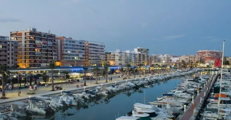 A marina with boats docked in front of buildings at dusk and Alicante property for sale.