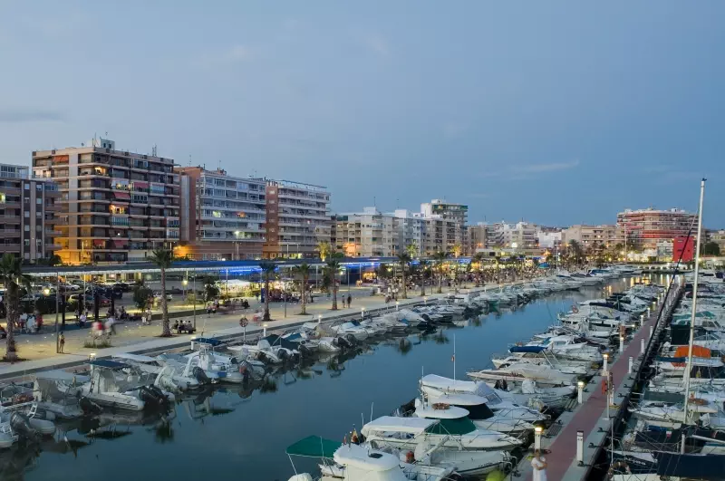 A marina with boats docked in front of buildings at dusk and Alicante property for sale.