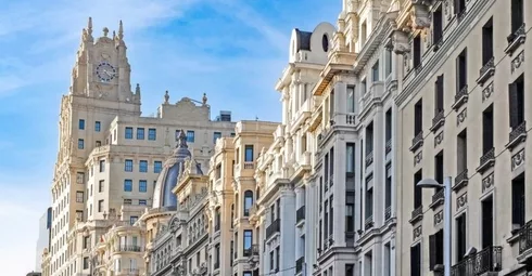 Madrid's city street showcases tall buildings and a prominent clock tower; one of the top 3 European cities to invest in.