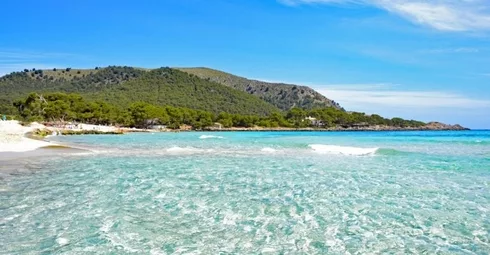 A top Spanish beach with clear water and a mountain in the background.