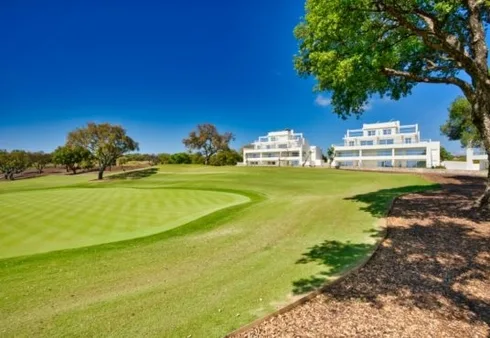 A golf course with trees and buildings in the background, located in Cadiz or San Roque.